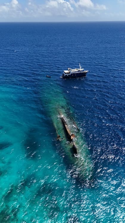 Una vista aérea del Truck Máster, el barco que llevó a los expedicionarios hasta el atolón bikini y más abajo se ven el pecio del buque de guerra alemán Prinz Eugen