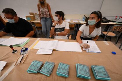 Una vista muestra las papeletas de votación para el referéndum constitucional y los oficiales de votación con una máscara facial y uno con guantes, en un colegio electoral en el centro de Roma el 20 de septiembre de 2020