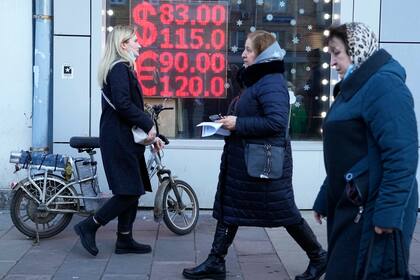  Unas personas caminan frente a una oficina de cambio de moneda que muestra el tipo de cambio del dólar y el euro a rublos rusos en Moscú, el 28 de febrero de 2022. 