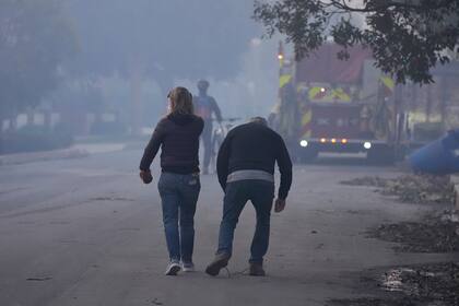 Unas personas caminan por una calle después de que un incendio devastó un vecindario en el vecindario Pacific Palisades de Los Ángeles, el jueves 9 de enero de 2025. (AP Foto/Damian Dovarganes)