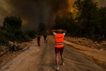 Unas personas corren lejos del poblado de Sirtkoy, en Antalya, Turquía, el domingo 1 de agosto de 2021, luego de que fue devastado por un incendio forestal. (AP Foto)
