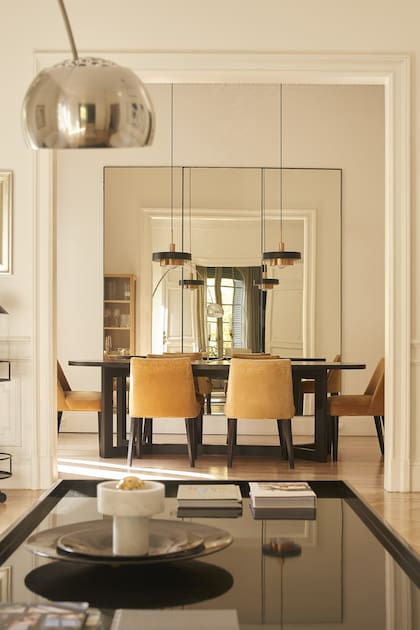 Unión sutil de tres paños de espejos para tomar gran parte del comedor. Artefactos colgantes ‘Acopla Doble’ en negro y cobre (Boutique de Luz).