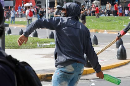 Uno de los agresores arroja una botella de vidrio vacía hacia los policías
