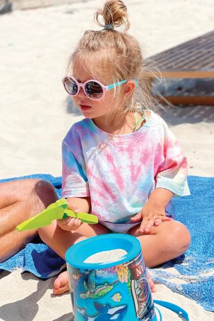 Valentina (2) en una postal de playa, muy trendy con anteojos y una remera batik para protegerse del sol
