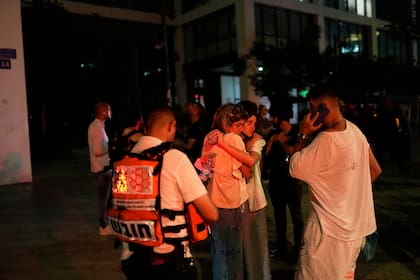 Varias personas aguardan y se apoyan mutuamente junto a un edificio alcanzado por un misil disparado desde Irán, el viernes 13 de junio de 2025, en Tel Aviv, Israel. (AP Foto/Tomer Appelbaum)