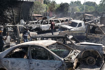 Varias personas buscan piezas rescatables de coches quemados en un taller mecánico incendiado durante la violencia desatada por pandillas armadas en Puerto Príncipe, Haití, el lunes 25 de marzo de 2024