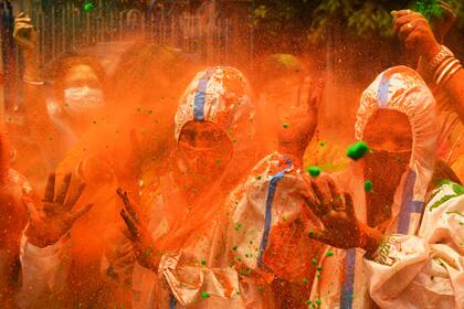 Varias personas que usan trajes protectores como medida preventiva contra la propagación del coronavirus, juegan con polvos de colores mientras celebran Holi