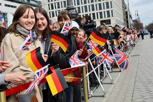 Varias personas sostienen banderas mientras esperan para saludar al rey Carlos de Inglaterra, en Berlín, Alemania, el 29 de marzo de 2023.
