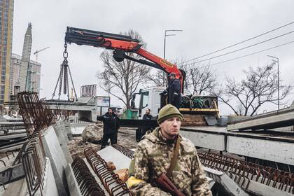 Varios operarios cargan losas de cemento frente a un miliciano ucraniano, en Kiev (Ucrania). Diego Herrera - Europa Press