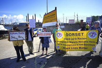 Varios simpatizantes sostienen una pancarta frente al puerto de Portland antes de que lleguen los primeros solicitantes de asilo para embarcar en la barcaza de alojamiento Bibby Stockholm, en Dorset, Inglaterra, el lunes 7 de agosto de 2023. (Ben Birchall/PA vía AP)