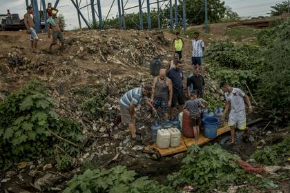Venezolanos juntan agua de un arroyo contaminado en Maracaibo