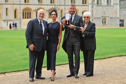 Vestido de jaquette, Beckam posa con su medalla. Junto a él, Lady Victoria optó por un diseño de su marca, en tono azul marino, con mangas cortas con aberturas laterales y drapeado en la parte frontal. También estuvieron junto al ex futbolista sus padres, David y Sandra