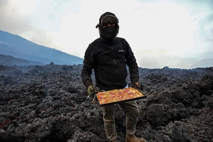 Vestido de pies a cabeza con ropa protectora para evitar quemaduras, acomoda la pizza sobre las rocas ardientes