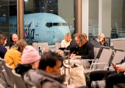 Viajeros aguardan en la terminal, mientras un avión de Alaska Airlines se sitúa en una puerta, en el Aeropuerto Internacional de Los Ángeles, en Los Ángeles, el 11 de enero de 2023
