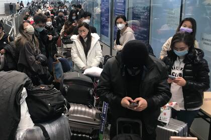 Viajeros esperan durante horas para subir a los autobuses que les llevarán a los hoteles e instalaciones en cuarentena del aeropuerto de Guangzhou Baiyun, en la provincia meridional china de Guangdong, el 25 de diciembre de 2022. 