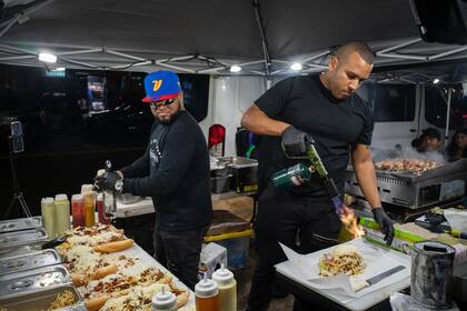 Víctor José Hernández hace los pepitos mientras su jefe, Marvin Ramírez, empuña un soplete para fundir el queso en una noche ajetreada en el Palacio De Los Pepitos.