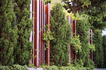 Vigas de hierro o madera en vertical entre el verde del cerco dan un aire artístico al jardín.