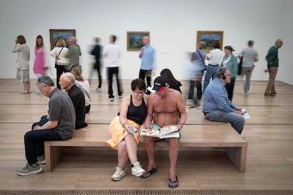 Visitantes en traje de baño se sientan en un banco mientras leen un libro durante la experiencia denominada "Día de los bañistas" inspirada en el artista italiano Maurizio Cattelan, con motivo de la exposición "Cézanne" del pintor francés Paul Cézanne en la Fundación Beyeler en Riehen, al norte de Suiza