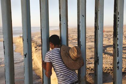 Vista al río. A la izquierda, un hombre observa a través de los barrotes de una cerca en la frontera de Tijuana, México