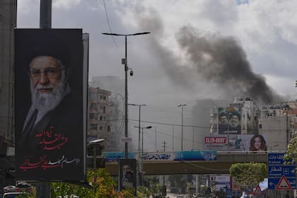 Vista de un retrato del difunto líder supremo de Irán, Ali Khamenei, y al fondo humo tras un ataque aéreo israelí en Dahiyeh, Beirut, Líbano, el otro frente de la guerra