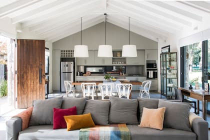 Vista del espacio integrado desde el living, con fofá de tres cuerpos con funda gris con almohadones de terciopelo (Good Luck Casa).