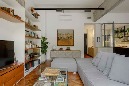 Vista desde el living, la cocina iluminada, a la derecha. El cerramiento de vidrio deja pasar más que la luz: la mirada atenta podrá advertir que la mesada de Carrara atraviesa la abertura en un elegante gesto de continuidad