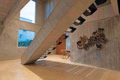 Vista general del hall de entrada, en el que se luce el combo protagonista de la planta: la escultural escalera con el tobogán. Junto a la escalera y acompañando la circulación hacia la biblioteca, una original obra de Pía Persia.