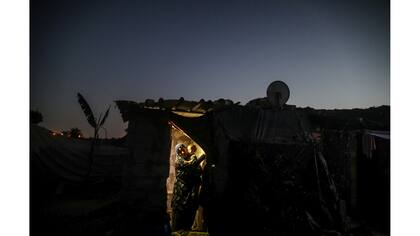 Una mujer con su hijo en brazos sale de su casa iluminada por una linterna durante un corte de luz en Khan Younis, en el sur de la Franja de Gaza