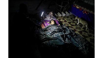 Una mujer discapacitada yace en una cama mientras un pariente la ilumina con una linterna para que el fotógrafo la vea durante un corte de luz en Khan Younis, en el sur de la Franja de Gaza