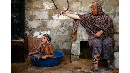 Una mujer palestina baña a su hijo con agua de un tanque, llenado por una organización benéfica, dentro de su vivienda en Khan Younis, en el sur de la Franja de Gaza