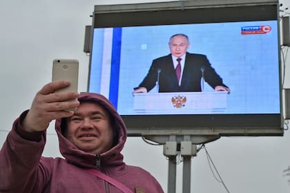 Un hombre se saca una selfie frente a una pantalla en Sebastopol, Crimea, que muestra a Putin durante un discurso en Moscú  