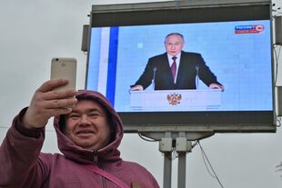 Un hombre se toma una selfie frente a una pantalla de televisión que muestra al presidente ruso, Vladimir Putin, durante su discurso anual sobre el estado de la nación en Sebastopol, Crimea, el martes 21 de febrero de 2023