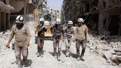 Voluntarios de protección civil de Siria, conocidos como los Cascos Blancos, caminan entre los escombros después de un ataque aéreo