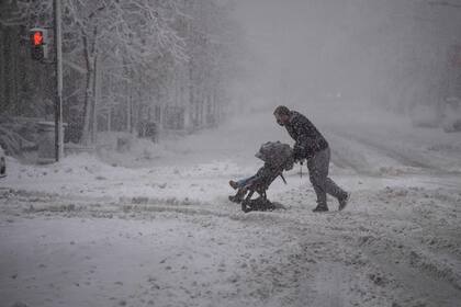 Un hombre con su bebé cruza una calle cubierta de nieve