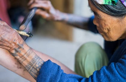 Whang Do concentrada en su labor, tatuando el brazo de uno de los tantos turistas que llegan hasta su pueblo para tatuarse con ella.