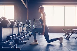 Woman doing lunges exercise with dumbbells in gym.