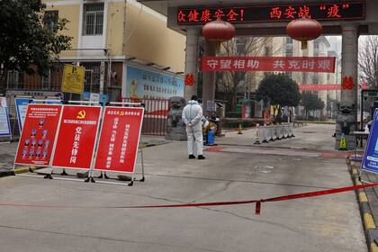 Un hombre vestido con equipo protector, monta guardia a la entrada de un edificio de Xi'an para hacer cumplir el confinamiento