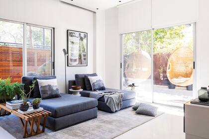 Sofás tipo chaise longe (Alma Deco BsAs) con almohadones (Agave) y manta (Valsen). Mesa de apoyo (Guadalupe Daffra) y lámpara ‘Consuelo’ (La Feliz).