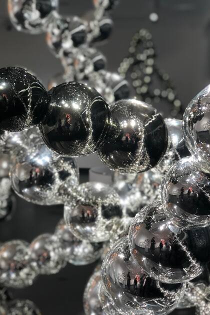 Todos esos collares, a su vez, se reflejan en el espejo que funciona como base de la obra y en los vidrios que separan la sala del pasillo, en un loop psicodélico que parece no tener final