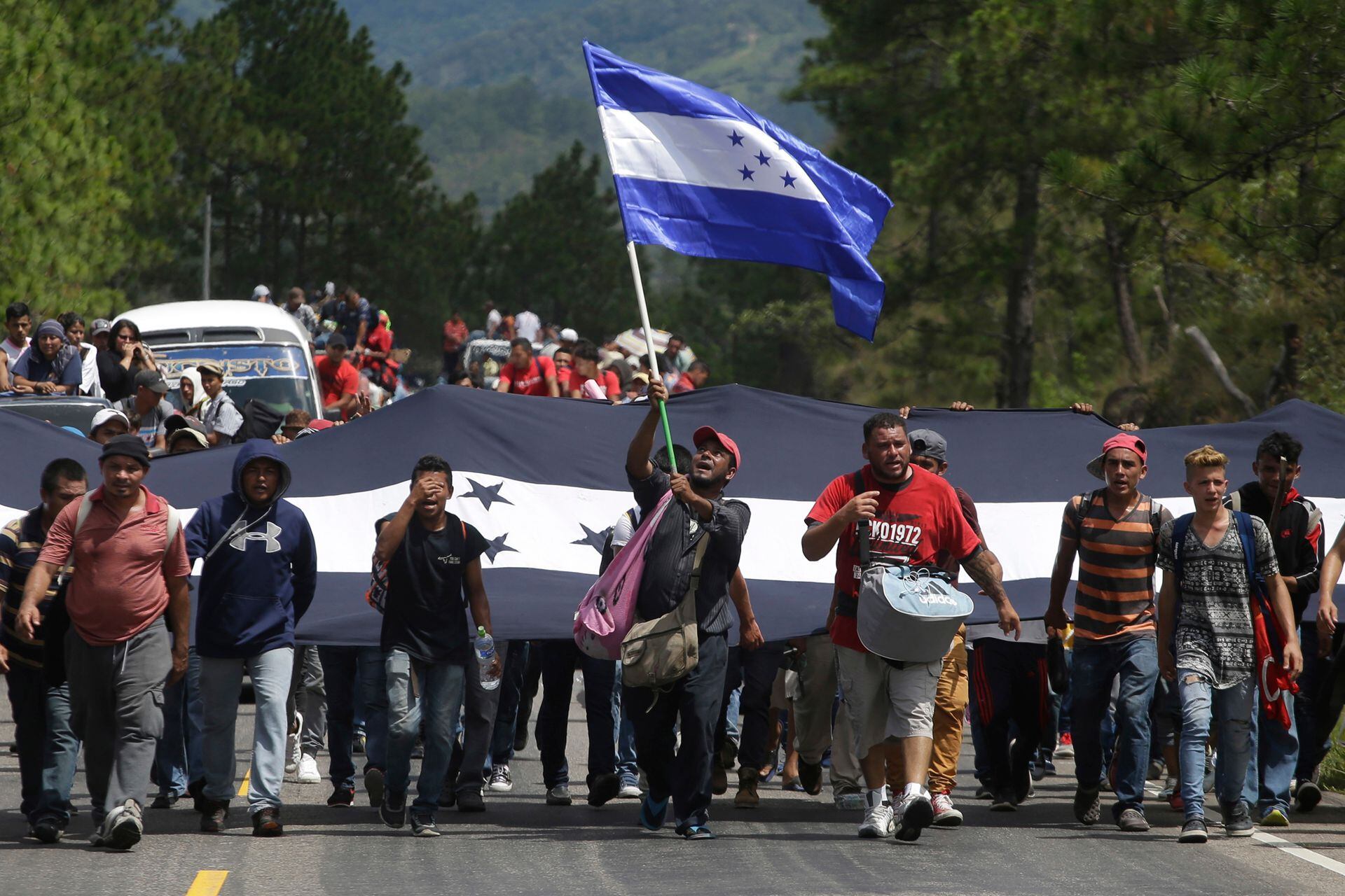 Los migrantes marchan por una ruta flameando la bandera de Honduras