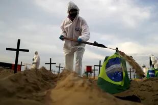 Un activista de la ONG Río de Paz, con un traje protector, cava tumbas en la playa de Copacabana para simbolizar a las víctimas del coronavirus