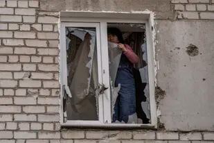 Una mujer coloca un plástico sobre los vidrios rotos de una ventana tras un ataque ruso en la víspera, en la zona residencial de Mikolaiv, Ucrania, el 29 de marzo de 2022. (AP Foto/Petros Giannakouris)