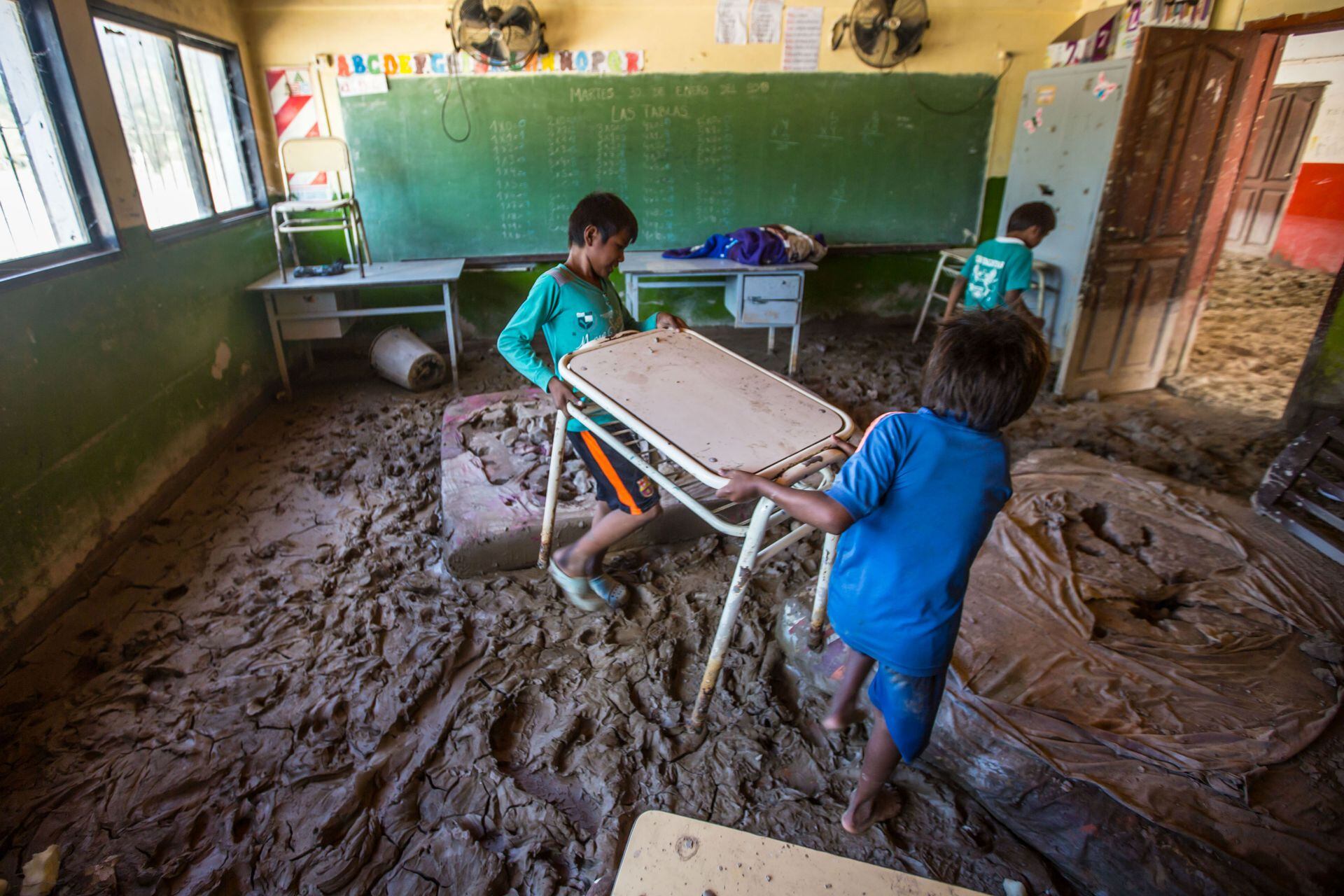 Dos chicos mueven un pupitre en su escuela llena de lodo