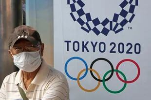 Un hombre usa una máscara higiénica mientras se sienta junto a un anuncio para promocionar los Juegos Olímpicos de Tokio 2020 