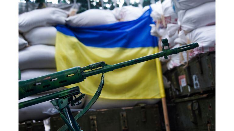 Un rifle de francotirador se coloca delante de la bandera de Ucrania en el pueblo de Marinka